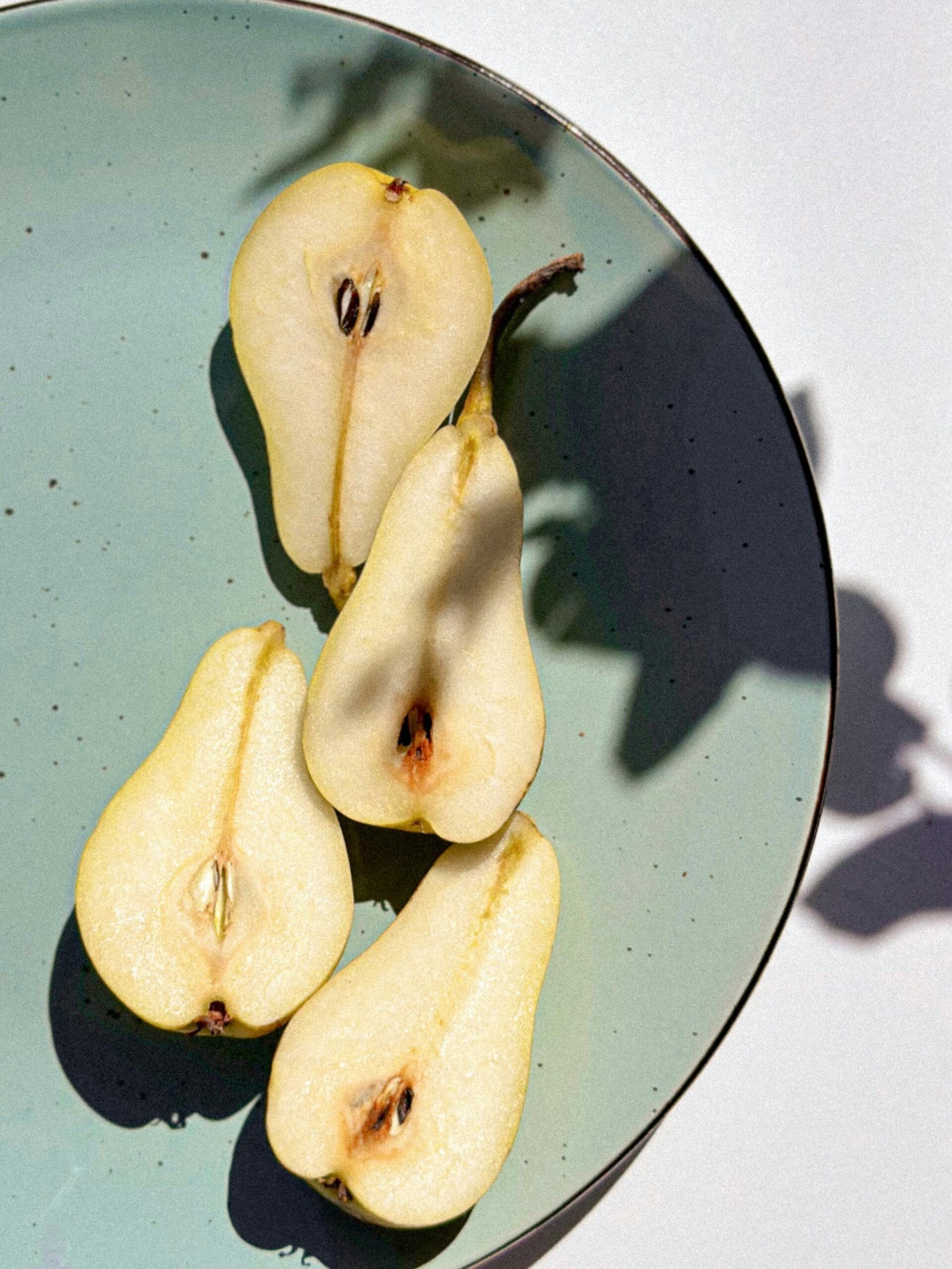 Sliced pears arranged on a green ceramic plate with natural shadows.