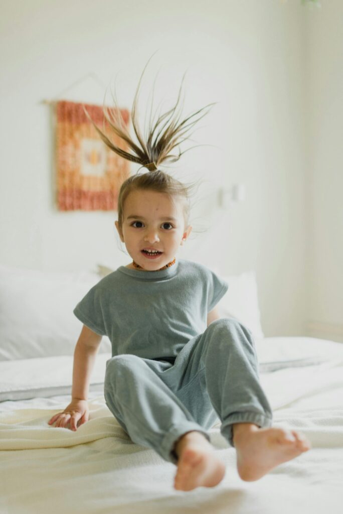 Adorable child with playful hair enjoying a carefree moment indoors, sitting on a cozy bed.