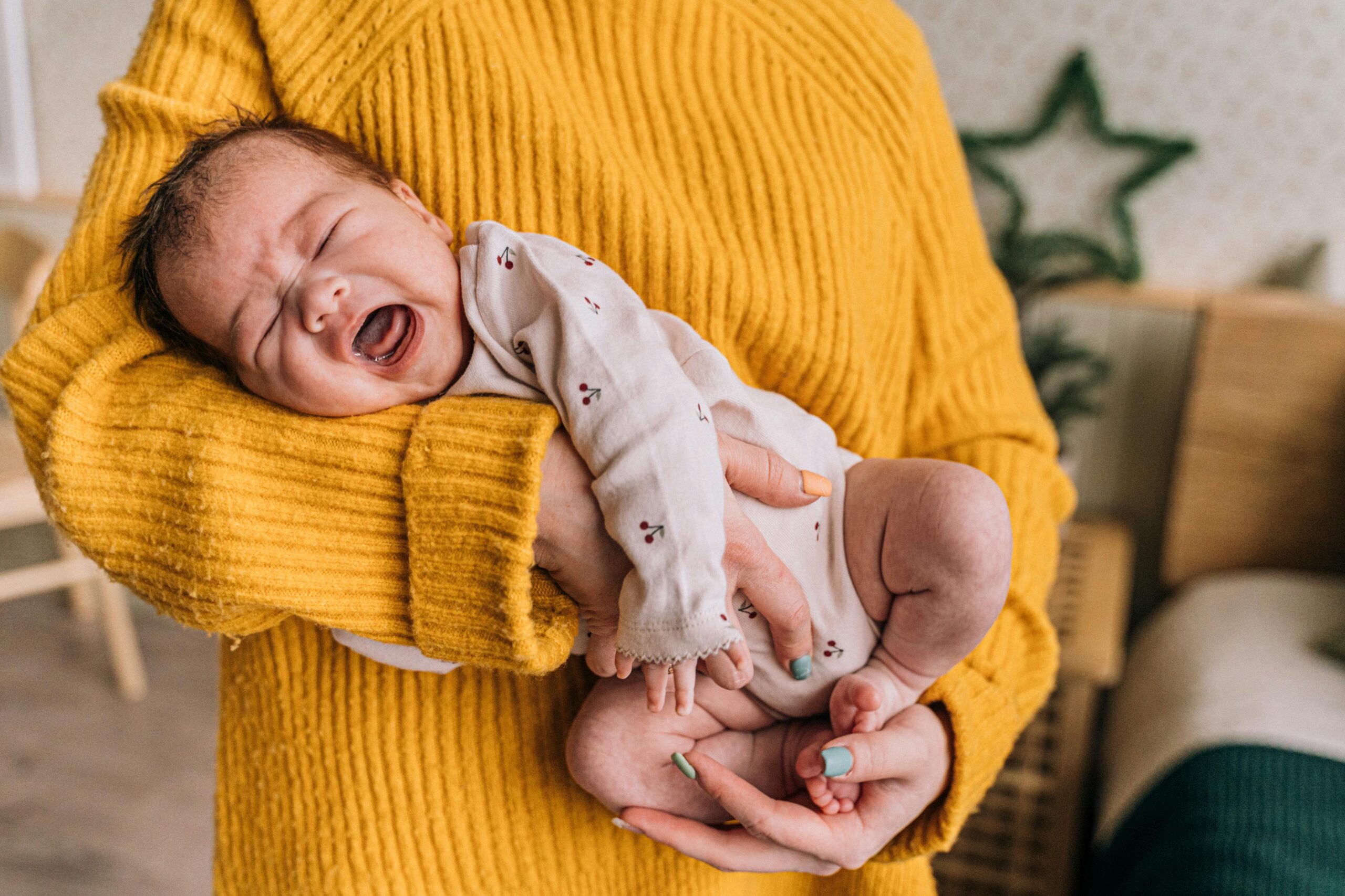 A mother gently holds a crying baby in her arms, providing warmth and comfort indoors.