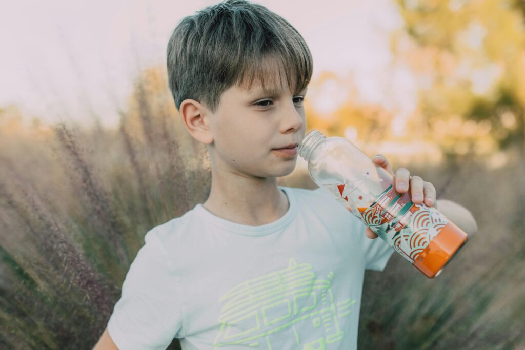 A young boy refreshes himself with a drink outdoors in a natural setting.